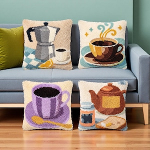 Peut inclure: Quatre coussins carrés avec des motifs en punch needle texturé. L'un présente une cafetière italienne, un autre une tasse de café fumante, un troisième une tasse rayée violette avec une cuillère, et le dernier une théière brune avec un pot et du pain.