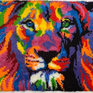 May include: A colorful, handmade rug featuring a lion's face. The lion's mane and face are depicted in a vibrant array of colors, including blue, orange, yellow, pink, and green, against a black background. The rug is made of yarn.