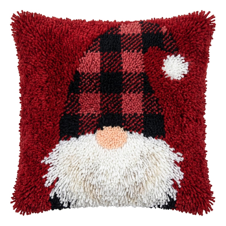 Puede incluir: Un coj&iacute;n cuadrado con un dise&ntilde;o texturizado de gnomo hecho con t&eacute;cnica de gancho. El gnomo lleva un gorro de cuadros rojos y negros con un pomp&oacute;n blanco y tiene una barba blanca grande y peluda sobre un fondo rojo oscuro s&oacute;lido.