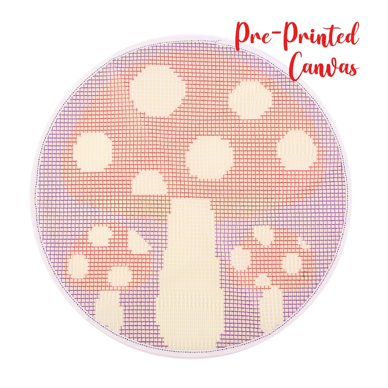 May include: A round, pre-printed canvas featuring a mushroom design. The mushroom has a red cap with white spots and a cream-colored stem. The background is a grid of purple and red threads, with the text "Pre-Printed Canvas" in red.