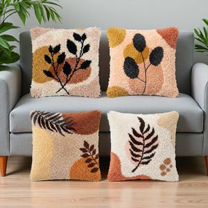 May include: Four square throw pillows featuring a textured, tufted surface with abstract botanical designs. The pillows display a color palette of cream, beige, mustard yellow, terracotta, and black, showcasing various leaf and branch patterns.