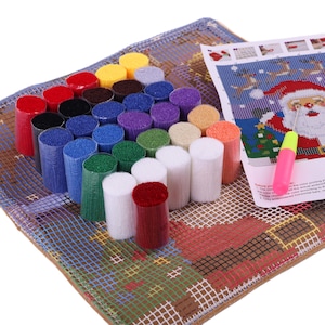 Puede incluir: Un kit de manualidades de gancho con un lienzo de rejilla que tiene un dise&ntilde;o de Pap&aacute; Noel impreso, una colecci&oacute;n de paquetes de hilo precortado en varios colores incluyendo rojo, azul, verde, blanco y amarillo, y un gancho con mango rosa.