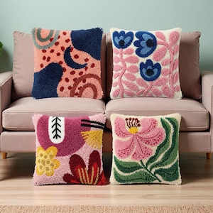 May include: Four decorative throw pillows with colorful, textured designs. The pillows feature abstract shapes, floral patterns, and a variety of colors including pink, blue, yellow, and green. They are arranged on a pink sofa.