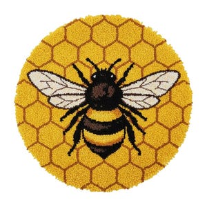 May include: A round, yellow rug with a bee design. The bee is black and yellow with white wings, centered on a honeycomb pattern. The rug is made of a textured material, likely wool or a similar fiber.