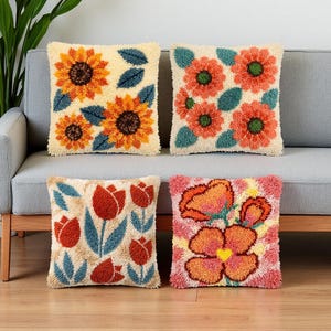 May include: Four square throw pillows featuring textured punch needle embroidery. The top left shows yellow sunflowers with blue leaves on cream. The top right has orange flowers with green centers. The bottom left displays red tulips. The bottom right shows large pink and orange flowers.