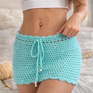 Pu&ograve; includere: Mini gonna all'uncinetto azzurra con bordo smerlato e vita con coulisse. La gonna &egrave; fatta a mano e presenta un motivo a punto strutturato. Il cordoncino ha perline decorative. La gonna &egrave; lunga circa 30 cm.