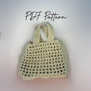 May include: A cream-colored, crocheted tote bag with a rectangular shape and a handle. The bag features an open, airy weave pattern. The text "PDF Pattern" is written in a cursive font above the bag.