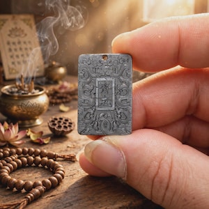 Puede incluir: Un colgante rectangular gris con intrincados patrones de volutas en relieve y un panel central vertical con caracteres chinos grabados. El colgante tiene un pequeño orificio en la parte superior para colgarlo y un acabado mate texturizado.