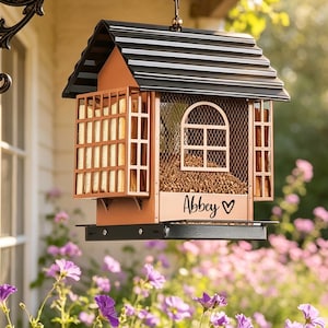 May include: A copper-colored bird feeder with a black roof and a mesh window. The feeder has a rectangular shape with a small tray at the bottom. The name "Abbey" is written on the front with a heart symbol.