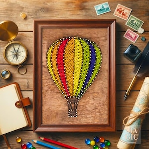 Puede incluir: Una pieza de arte de hilo enmarcada representa un globo aerostático colorido sobre un fondo de madera. El globo presenta secciones rojas, naranjas, amarillas, verdes y azules. La escena incluye una brújula, sellos, un cuaderno y un mapa, sugiriendo un tema de viaje.