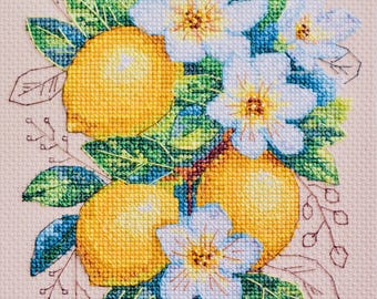 Puede incluir: Bordado de punto de cruz de limones amarillos, flores blancas y hojas verdes. Los limones son amarillos, las flores son blancas con centros amarillos y las hojas son de varios tonos de verde y azul. El fondo es de color beige claro.