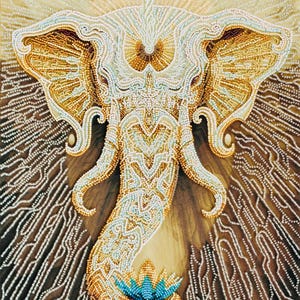 Op de afbeelding: Gedetailleerd kralenkunstwerk van een olifantenkop, met ingewikkelde patronen in goud, wit en turquoise. De slurf van de olifant buigt naar beneden en eindigt in een lotusbloem. De achtergrond heeft een bruin en wit patroon.