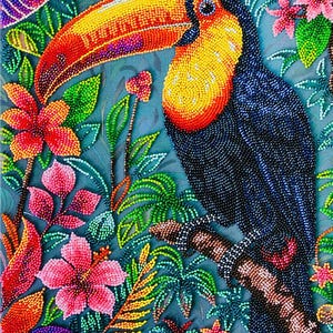 May include: A vibrant beaded artwork featuring a toucan perched on a branch amidst lush tropical foliage. The toucan has a large yellow and orange beak, with a black body and a yellow chest. The background is a teal color, with colorful flowers and leaves.