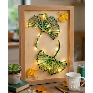 Peut inclure: Une œuvre d'art encadrée en fil, représentant deux motifs de feuilles de ginkgo en vert et jaune, illuminés par de petites lumières. L'œuvre est placée sur un fond en bois clair dans un cadre en bois naturel. Des accents décoratifs en fil jaune sont également présents.