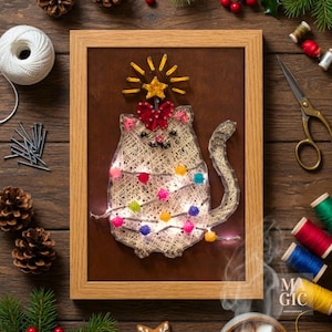 Puede incluir: Una pieza de arte de hilo enmarcada que presenta un gato decorado como un árbol de Navidad. El gato está hecho de hilo blanco con luces de colores, un lazo rojo y una estrella en la parte superior. El marco es de color marrón claro.