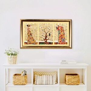 K&ouml;nnte beinhalten: Ein gerahmter Triptychon-Kunstdruck mit einem goldfarbenen Kunstwerk mit einem Baum und Figuren. Das Kunstwerk befindet sich in einem goldenen Rahmen und wird &uuml;ber einem wei&szlig;en Regal mit dekorativen Gegenst&auml;nden ausgestellt.