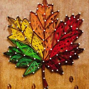 Peut inclure: Une feuille d'érable en art de ficelle faite à la main, aux couleurs automnales : vert, jaune, orange et rouge. La feuille est montée sur un fond en bois et ornée de petits clous argentés. Des perles de verre décoratives pendent en dessous.