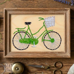 May include: A framed string art piece featuring a green bicycle with a basket. The bicycle is crafted with green string, white string for the wheels, and black string for the tires. The frame is made of wood.