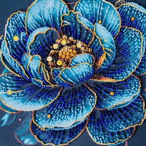 May include: Close-up of a beaded floral design. The flower features shades of blue and gold beads, with a dark blue background. The petals are outlined in gold, and the center is a cluster of golden beads.