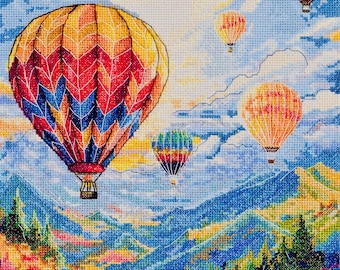 Könnte beinhalten: Ein Kreuzstichbild mit bunten Heißluftballons, die über einer Berglandschaft schweben. Die Ballons weisen lebendige Muster in Rot, Gelb, Blau und Grün auf. Die Berge und der Vordergrund sind mit detaillierten Stichen gefüllt.