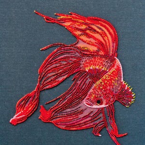Puede incluir: Una detallada obra de arte con cuentas de un pez Betta rojo, también conocido como pez luchador siamés, sobre un fondo verde azulado oscuro. El pez presenta un intrincado trabajo de cuentas en tonos de rojo, naranja y amarillo, con aletas y cola fluidas.