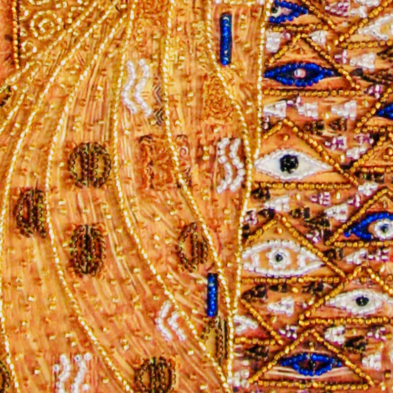 K&ouml;nnte beinhalten: Nahaufnahme eines detaillierten Textils mit aufwendiger Perlenarbeit. Das Design zeigt goldene, orangefarbene und wei&szlig;e Perlen mit blauen Akzenten. Das Muster umfasst Augenmotive und geometrische Formen.