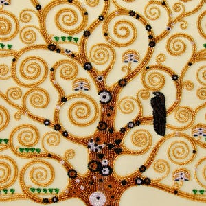 K&ouml;nnte beinhalten: Nahaufnahme eines Perlenkunstwerks, das einen stilisierten Baum mit goldenen Spiralzweigen und einem braunen Stamm darstellt. Der Baum ist mit schwarzen und wei&szlig;en Akzenten und kleinen, pilzartigen Details verziert. Der Hintergrund ist hellbeige.