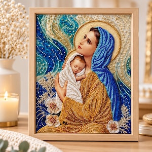 May include: A framed diamond painting depicting a woman in a blue head covering holding a baby wrapped in a white cloth. The artwork features a gold halo, a golden yellow garment, and a swirling blue and white background with floral accents.
