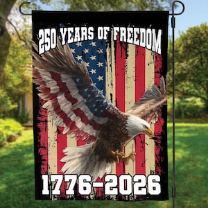 Op de afbeelding: Een tuinvaandel met een Amerikaanse vlag en een Amerikaanse zeearend. De vlag heeft de tekst "250 YEARS OF FREEDOM" en "1776-2026" in het wit. De vlag wordt buiten weergegeven.