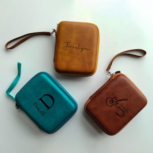 May include: Three personalized zippered cases in shades of brown and teal. The brown case has the name "Joselyn" in script. The teal case has the letter "D" and the name "Daniell". The other brown case has a guitar graphic and the name "Danielle".