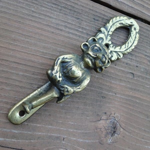 May include: A brass doorstop shaped like a monkey with a leafy design. The monkey is holding a stick and has a whimsical expression.