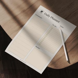 Peut inclure: Un planificateur quotidien crème avec les mots "Daily Planner" en haut. Le planificateur comprend des sections pour l'horaire, la liste des tâches, la date et les notes. Un crayon blanc repose sur le planificateur, sur une surface en bois.