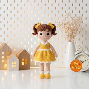 May include: A handmade crochet doll with brown hair styled in pigtails, adorned with yellow bows. The doll wears a yellow dress with white trim, yellow shoes, and white socks. The doll is standing on a white surface.