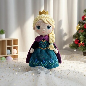 May include: A handmade crochet doll of a princess with blonde hair in a braid, wearing a teal dress with embroidered details, a purple cape, and a gold crown. The doll is approximately 12 inches tall.