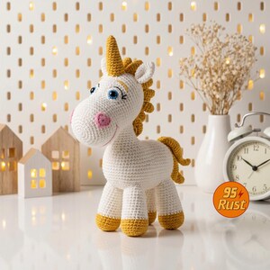 May include: A handmade crochet unicorn toy. The unicorn is white with a yellow horn, mane, and tail. It has blue eyes, pink cheeks, and yellow hooves. The toy is standing on a white surface.