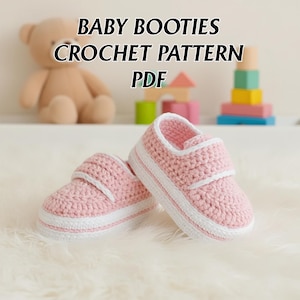May include: Pink crochet baby booties with white detailing and a velcro strap. The image includes the text "BABY BOOTIES CROCHET PATTERN PDF". The booties are displayed on a white, fluffy surface.