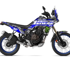 Può includere: Una moto Yamaha Ténéré 700 blu, argento e nera con il numero 32 sul lato. La moto ha un design delle ruote blu e nero e le parole "WORLD AID TENERE 700" sono visibili sul lato.