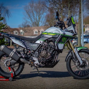 May include: A Yamaha motorcycle with a custom design featuring white, black, and green accents. The motorcycle has the "Monster" logo and "Yamaha" branding. It is parked on a paved surface.