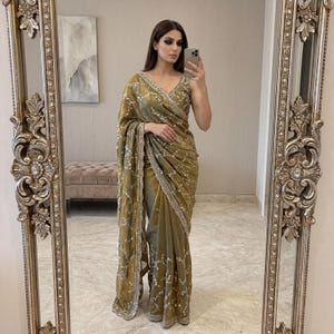 Peut inclure: Un sari de couleur or avec des broderies et des ornements argentés complexes. Le sari présente un design encolure en V et un style drapé, un vêtement traditionnel sud-asiatique. Le tissu a un éclat subtil.