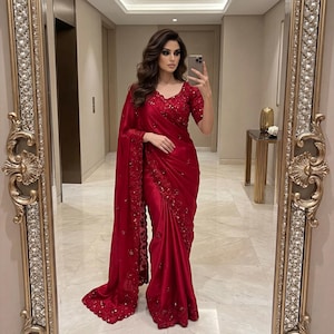 May include: A vibrant red saree with intricate embroidery and embellishments. The saree features a flowing drape, detailed border, and matching blouse. The elegant design is suitable for special occasions.