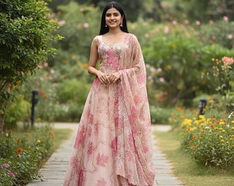 May include: A light pink floral print gown with a matching shawl. The gown features a scoop neckline and a full skirt. The shawl is draped over the shoulders. The dress is adorned with pink floral patterns and sequins.