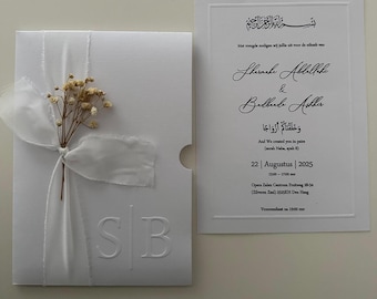 May include: White wedding invitation with embossed initials "SB" and a ribbon tied around dried flowers. The invitation includes text in multiple languages, including Arabic and English, with the date August 22, 2025.
