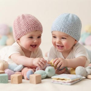 May include: Two knit baby hats, one in dusty pink and one in light blue, both featuring a textured chevron pattern and a ribbed brim. The hats are worn by two infants who are playing with various soft plush toys and wooden blocks on a flat surface.