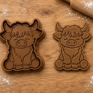 May include: A brown plastic cookie cutter shaped like a Highland cow with shaggy fur and horns, positioned next to a matching Highland cow shaped cookie. The design features a seated calf with closed eyes and a detailed snout and fur texture.