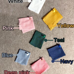 May include: A collection of fabric swatches in various colors, including white, pink, yellow, teal, blue, deep pink, and navy. Each swatch is pinned to a neutral surface and labeled with its corresponding color name.
