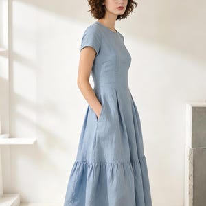 Pu&ograve; includere: Un abito azzurro con maniche corte e gonna a balze. L'abito presenta un corpetto aderente, uno scollo tondo e tasche. Il tessuto sembra essere un materiale leggero, adatto alle temperature pi&ugrave; calde. L'abito &egrave; in tinta unita.