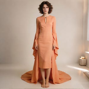 May include: A peach-colored dress with long sleeves and a flowing train. The dress features a keyhole neckline and flared sleeves. The skirt has a high slit, and the train extends from the back of the dress. The dress is made of a lightweight fabric.
