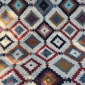 May include: A close-up of a patterned rug with a geometric design. The rug features a repeating diamond pattern in shades of red, blue, teal, brown, and gold on a neutral background. The text "Jaypore Carpet" is visible.