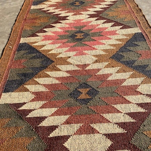 May include: A long, rectangular rug with a geometric pattern in shades of brown, red, pink, and cream. The rug features a repeating diamond design with a textured appearance, suitable for a hallway or entryway.