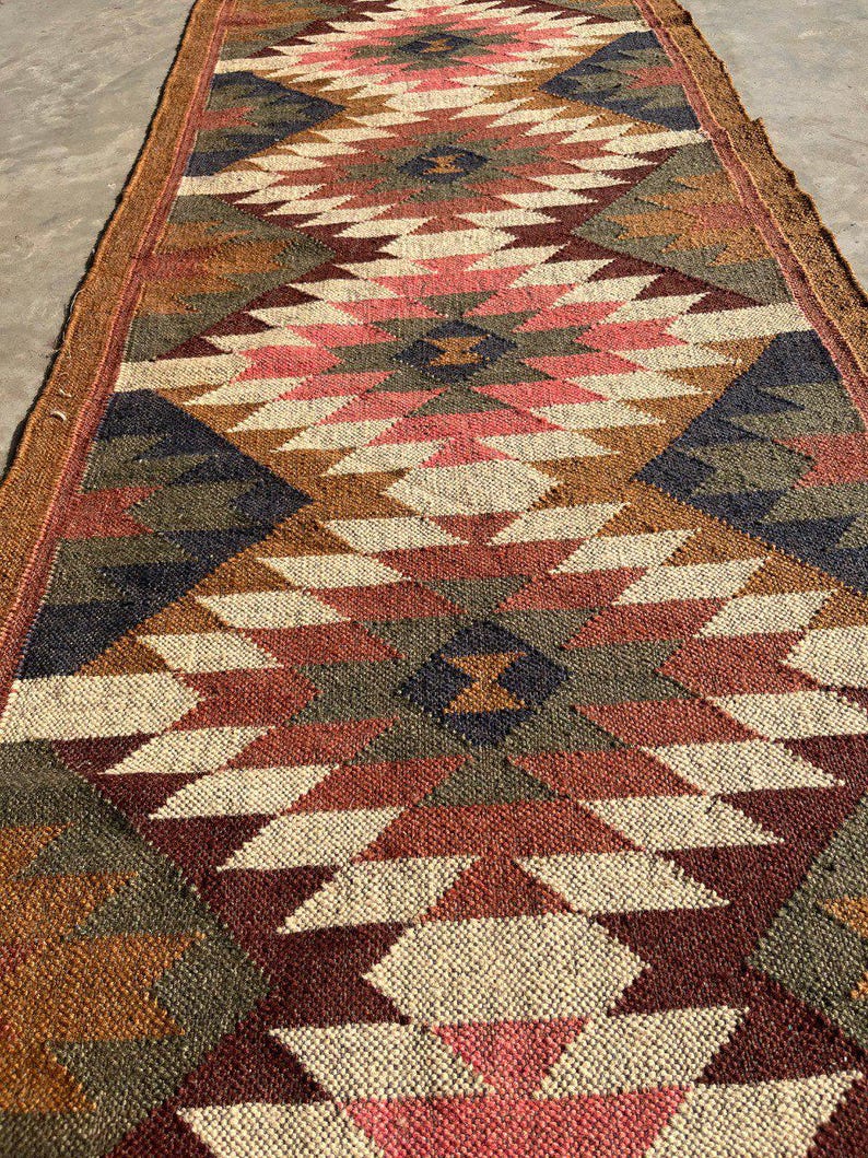 May include: A long, rectangular rug with a geometric pattern in shades of brown, red, pink, and cream. The rug features a repeating diamond design with a textured appearance, suitable for a hallway or entryway.